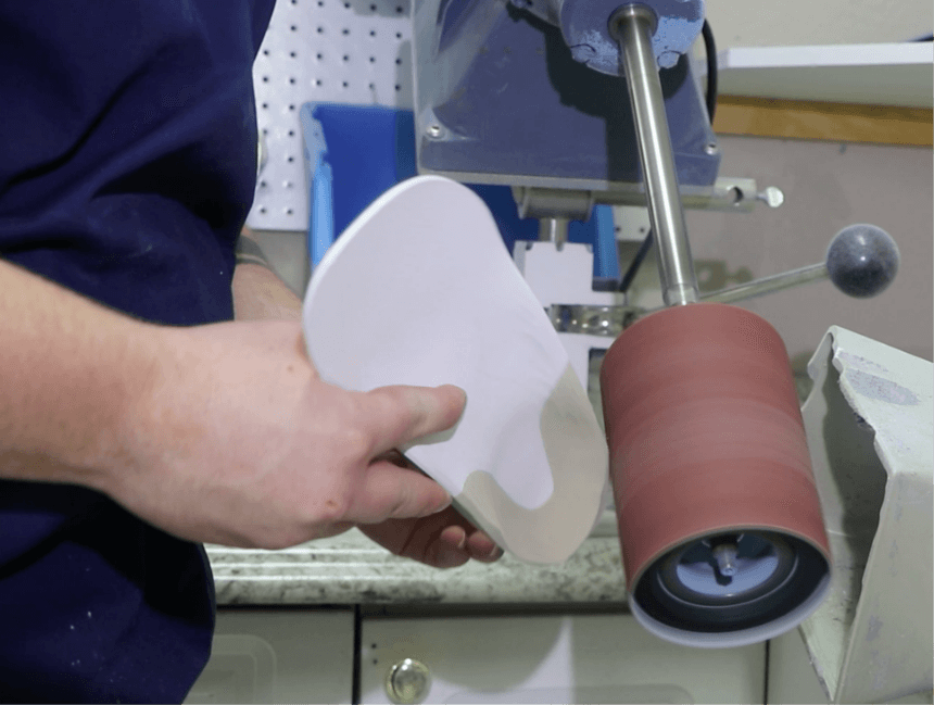 Person holding a custom orthotic foot pad and refining it with a specialized sanding machine, highlighting the durable, medical-grade craftsmanship engineered to provide long-lasting comfort and support for years