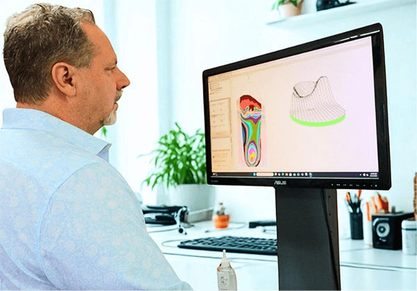 Expert podiatrist and orthotist reviewing custom foot orthotic design software showing a detailed foot drawing on screen, representing over 25 years of experience crafting corrective and supportive orthotics tailored to each patient’s needs